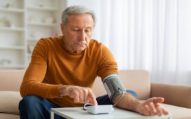 Elderly,Man,Sitting,On,Couch,,Checking,His,Blood,Pressure,With